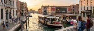 A panoramic view of students in Venice, Italy, featuring a water bus (Vaporetto) on the Grand Canal and Emisa Academy branding, illustrating student life and accommodation at Ca' Foscari University."